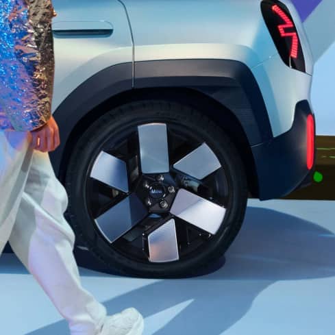 Closeup view of the 20” Concept Wheels on the MINI Concept Aceman, parked on a light blue surface with a man in white pants walking by.