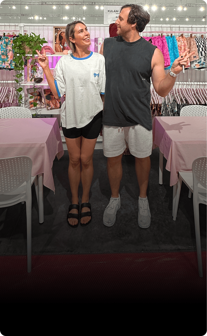 Dani Atkins and Alex holding up peace signs in front of a Kulani Swim pop up. 