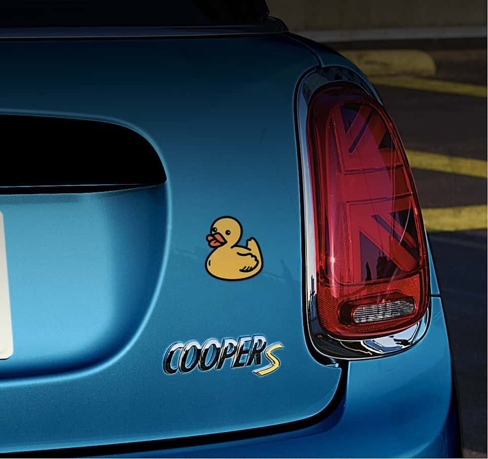 Close-up view of a taillight on the rear of a blue MINI, with a duck decal above “Cooper S” lettering.