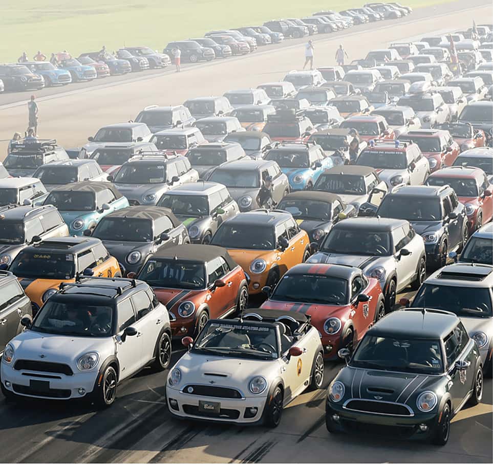 Overhead view of several MINIs parked in a grid style near a dirt path, with a faded background.