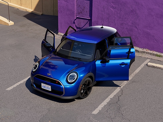 Birds-eye view of the MINI Cooper S 4 Door in Icy Sunshine Blue parked on a concrete surface with all four doors open and a purple concrete wall in the background.