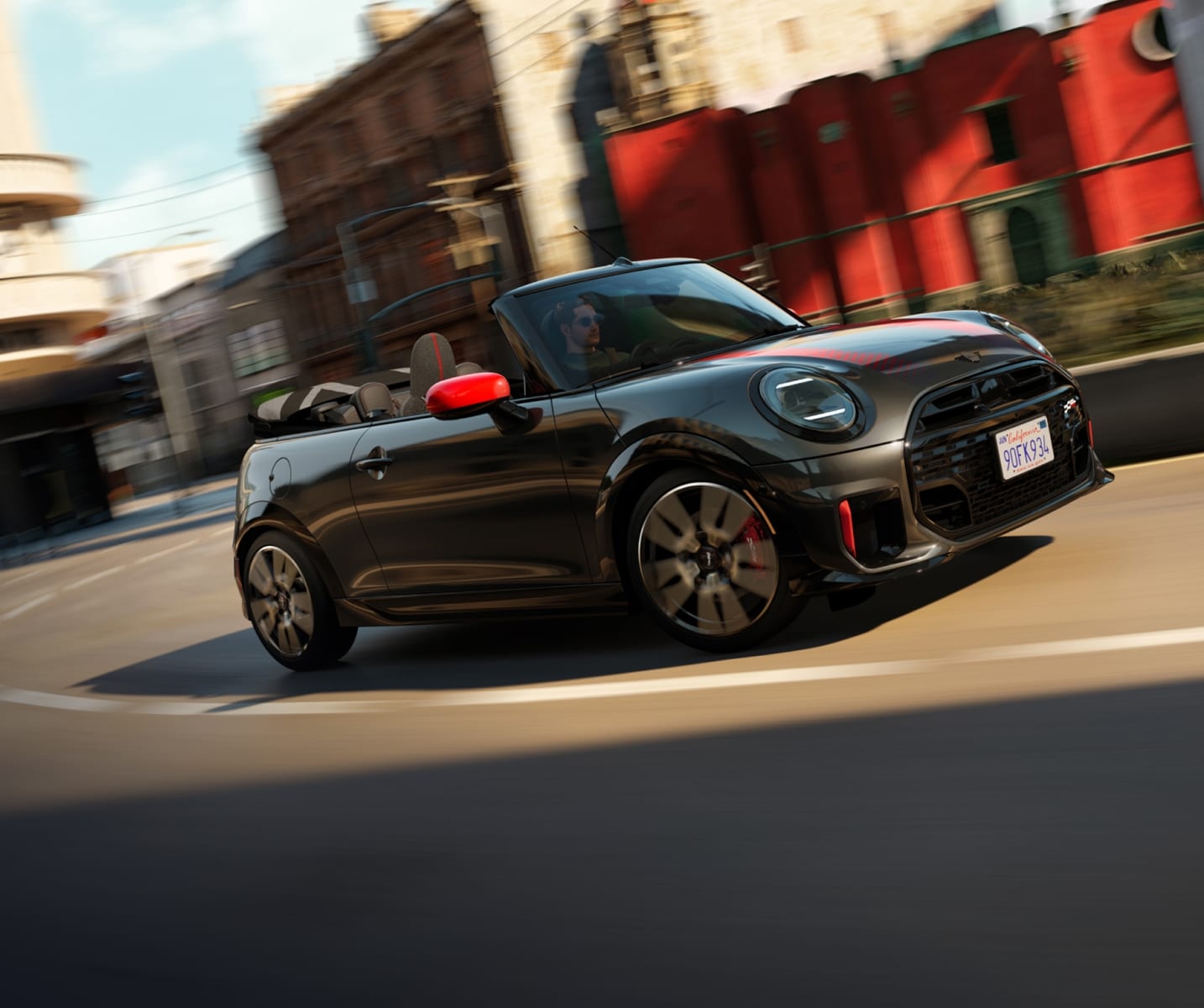 A MINI JCW Convertible rounding a bend with the top down in a city environment.