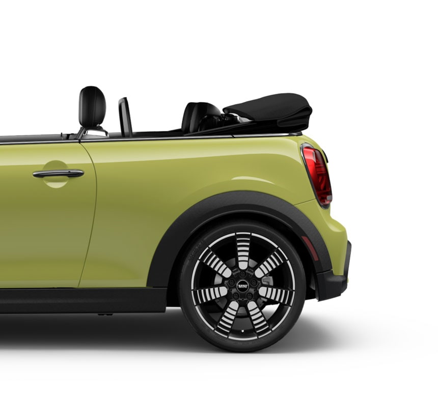Side view of the rear of a yellow MINI Convertible parked on a blank white surface with its shadow underneath and nothing in the background.