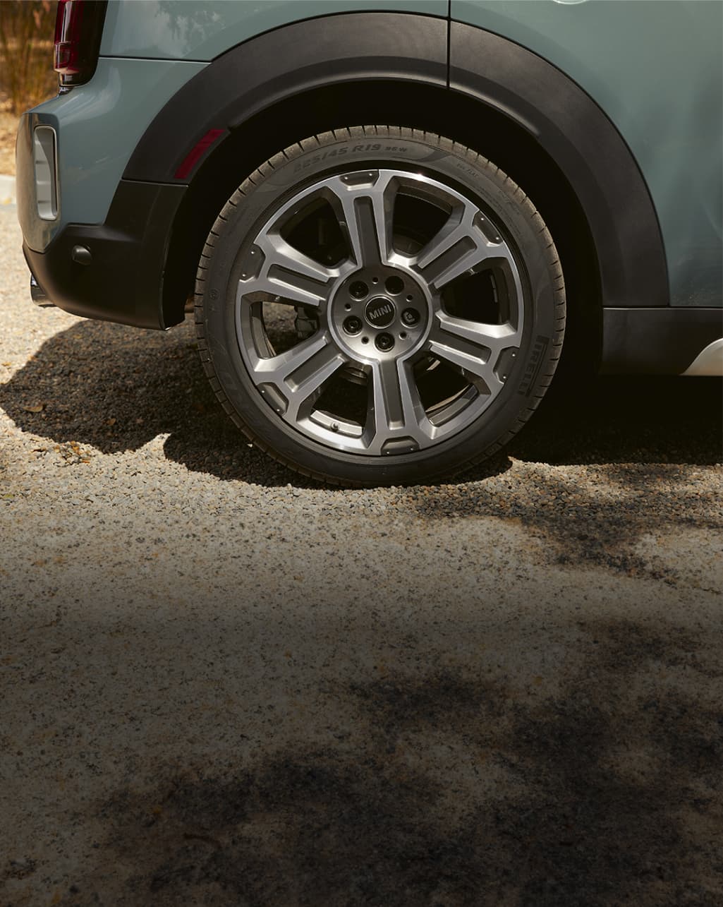 Closeup view of a wheel on a dark green MINI Countryman, parked on a pavement surface.