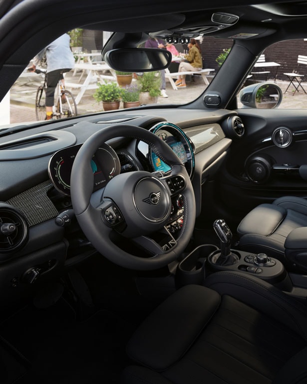 Closeup view of the steering wheel and dashboard inside a MINI Hardtop 4 Door from the perspective of the front passenger’s seat.